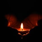 Close-up of hands warmly embracing a lit candle in the dark, creating a cozy atmosphere.