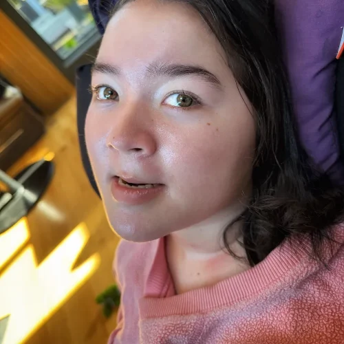 Iris at 18, seated in her supportive wheelchair, looking toward the camera