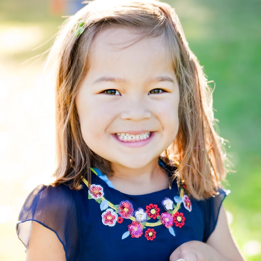 Iris, a young girl with GM1 gangliosidosis, smiling outdoors