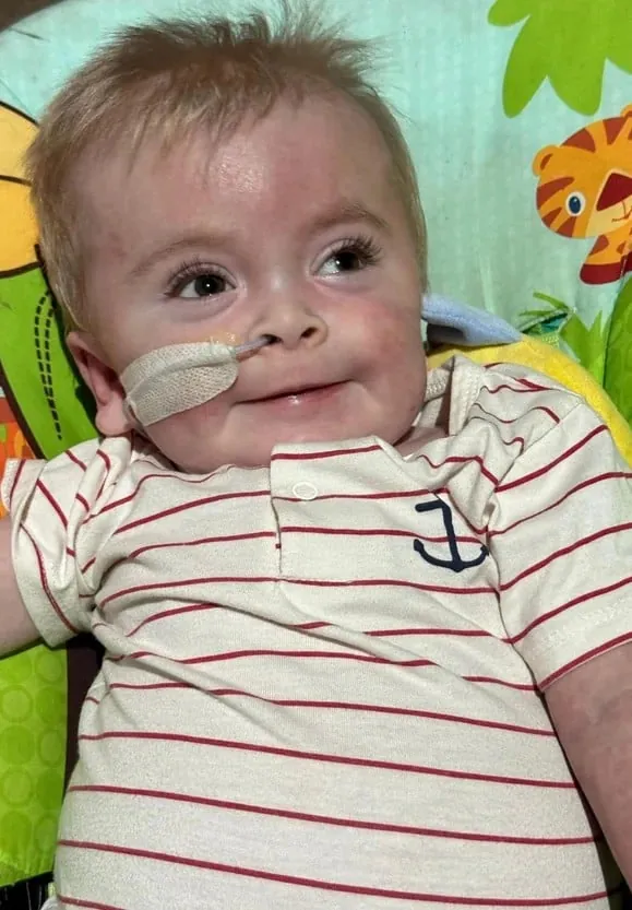 Milo, a young boy with GM1, smiling in a bouncer seat